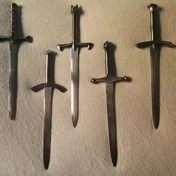 Cinque athame di acciaio appesi a una parete chiara