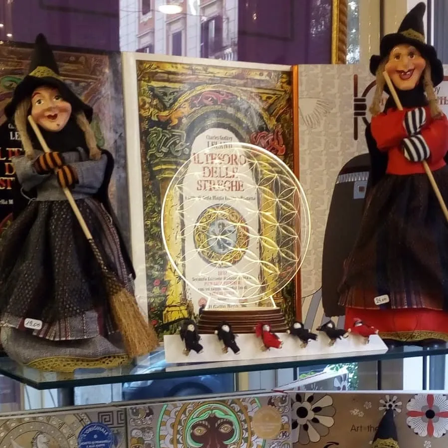 Un libro sulle streghe in vetrina tra due bambole di befana